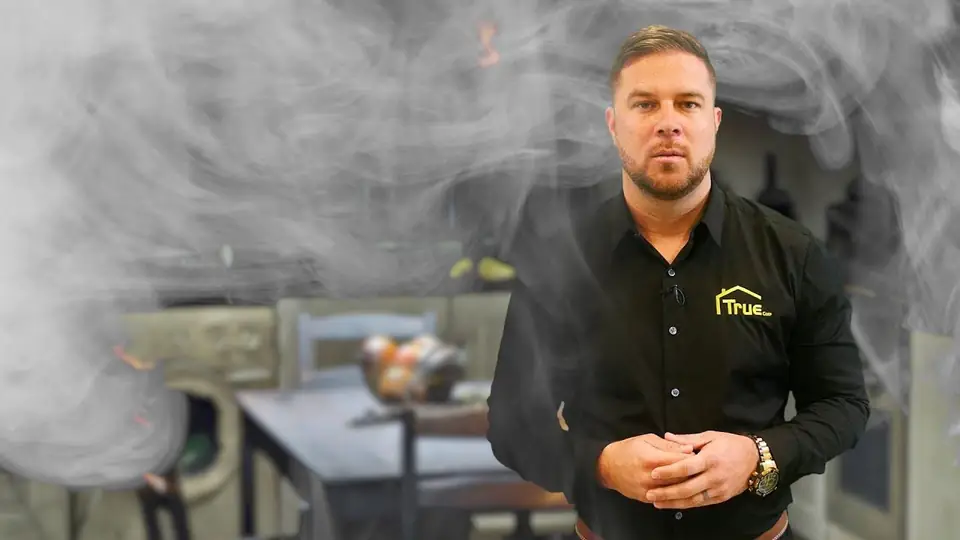 Smoke drifting through a fire-damaged dining room with a True Builders technician standing in it